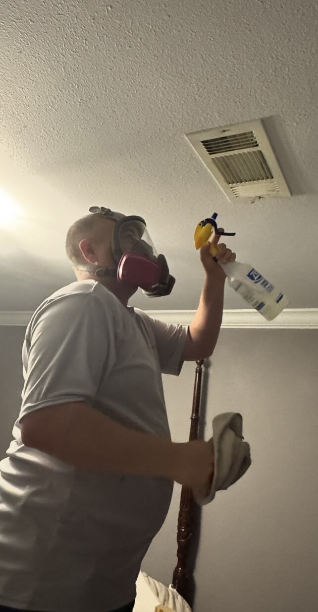 A Mold Shield Restoration technician in a respirator treating a ceiling air vent